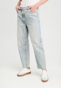 Lyseblå, højtaljede jeans med afslappet pasform, der har sømdetaljer og fem-lommemodel, parret med hvide og brune sneakers.