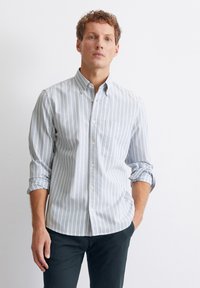 Camicia button-up a maniche lunghe di colore azzurro chiaro con strisce verticali bianche, dotata di taschino sul petto e colletto classico. Tessuto di cotone.