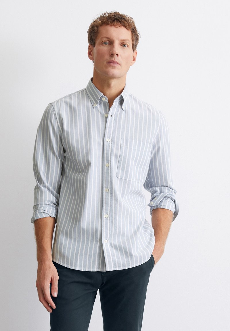 Camicia button-up a maniche lunghe di colore azzurro chiaro con strisce verticali bianche, dotata di taschino sul petto e colletto classico. Tessuto di cotone.
