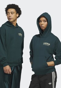 Tmavě zelené mikiny s kapucí vyrobené z měkké látky, se předními kapsami a zlatým logem "adidas" na hrudi.