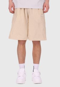 Shorts beiges avec un motif de grille texturé, taille élastique, poches latérales et petit logo blanc. Portés avec des baskets blanches et des chaussettes.