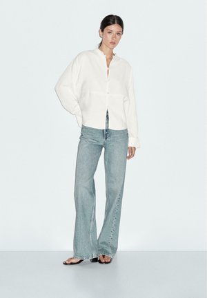 White button-up shirt with a collar, paired with light blue flared jeans. Soft texture, relaxed fit, and simple design details.