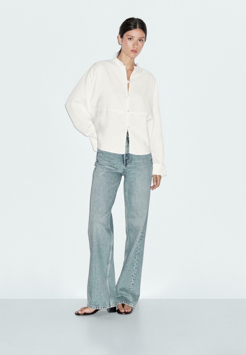 Vit skjorta med krage, parat med ljusblå utsvängda jeans. Mjukt material, avslappnad passform och enkla design detaljer.