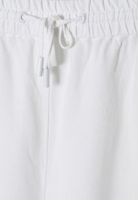 Pantalons légers blancs avec une taille froncée, une fermeture à cordon de serrage et une texture lisse. Présente un design minimaliste et des détails de couture subtils.