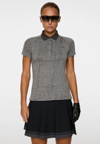Grijze textuur polo shirt met een zwarte kraag, gecombineerd met een geplooide zwarte rok. Zwarte handschoenen en zonnebril maken de outfit compleet.