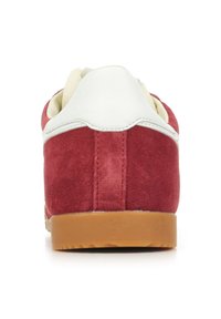 Zapatilla de ante roja con una lengüeta de cuero blanco en el talón y una suela de goma. Presenta una forma redondeada y detalles de costura visibles.