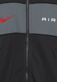 Close-up of black and gray jacket front with black zipper, red Nike swoosh on left, and white "AIR" text on right chest.