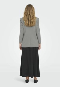 Blazer gris con rayas diplomáticas de manga larga combinado con una falda maxi negra. Telas suaves y corte tapered, con una abertura en el dobladillo trasero.