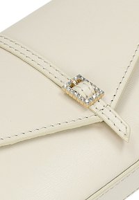 Crème leren handtas met een geometrisch ontwerp, versierd met een gouden gesp die is geaccentueerd met heldere stenen. Duidelijke stikseldetails.
