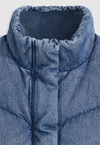 Denim puffer krage med quiltet tekstur, i en lys blå farge og myk innerforing, som fremhever en polstret, varm design.