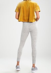 Žlutý sametový crop top s krátkými rukávy, spárovaný se světlými šedými, decentně upnutými legínami a šedými sportovními botami. Měkká textura a pohodlný design.