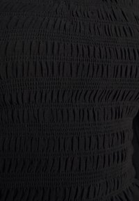 Tissu noir à smocks avec des fronces horizontales, présentant une surface texturée et des plis régulièrement espacés. Aucun élément métallique ou ornement visible.