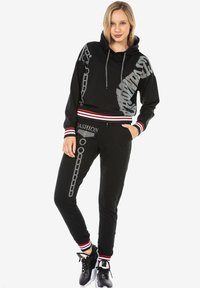 Schwarzes Hoodie- und Hosen-Set mit silbernem Kettenmuster und dem Text "FASHION". Mit roten und weißen Streifenakzenten an den Bündchen und am Bund.