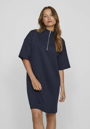 Vestido sobre tamaño azul marino de algodón suave con un cuello alto y mangas cortas. Presenta un cierre de media cremallera en la parte delantera y un corte holgado.