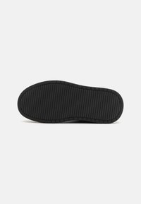 Black rubber shoe sole with a textured surface, featuring horizontal and vertical grooves for traction and durability. Rounded toe design.