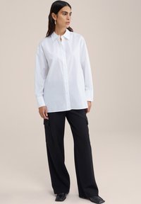 Camicia bianca a maniche lunghe con bottoni, caratterizzata da un colletto classico e una vestibilità comoda. Abbinata a pantaloni cargo neri a gamba larga con tasche.