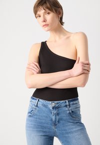 Bodysuit negro de canalé de un solo hombro combinado con jeans de mezclilla azul claro de corte clásico, con bolsillos frontales y un leve desgastado.
