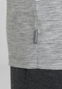 Grå kortärmad skjorta med texturerad yta, som har en sydd fåll och en liten märkesetikett nära sid sömmen.