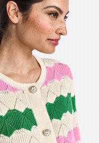 Knit cardigan, jossa on kerma-base ja vaaleanpunaisia sekä vihreitä tekstuurikuvioita, pyöreä kaula-aukko ja koristeelliset kukkabuutit.