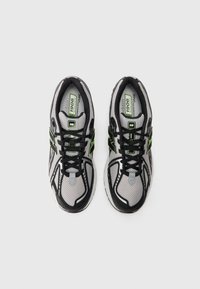Paire de chaussures de running New Balance 1906 grises, noires et vertes vues de dessus avec des lacets noirs sur un fond gris clair.