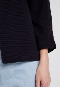 Mörk marinblå ribbad topp med 3/4 ärmar, avslappnad passform och en texturerad yta, kombinerad med ljusblå denim.