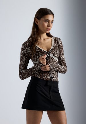 Leoparditrükkiga pikad varrukad särk, millel on pitsäär ja ees sidumisdetail, koos musta mini-seeliku ja sobitamisega. Särgil on kehasse sobiv v-kaelus.