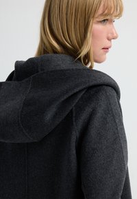 Abrigo de lana gris oscuro con capucha, textura suave y un diseño sencillo. El cuello se ajusta cómodamente alrededor del cuello.