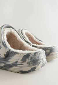 Chaussons à enfiler gris et blanc à motif, avec une doublure intérieure douce et moelleuse et une forme arrondie. Caractérisés par une semelle texturée pour une meilleure adhérence.