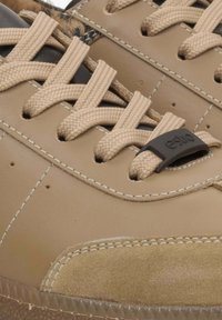 Bruine leren sneaker met tan suede accenten, voorzien van beige veters, een rubberen zool en contrasterende stiksels nabij het teengebied.