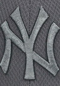 Grau fabric Kappe mit einem erhabenen, silbernen, gestickten "NY"-Logo. Der strukturierte Hintergrund zeigt ein diagonales Muster.