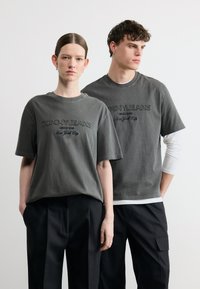 Δύο μοντέλα φοράνε ταιριαστά ξεθωριασμένα μαύρα t-shirts Tommy Jeans και μαύρο παντελόνι, με φόντο απλό λευκό.