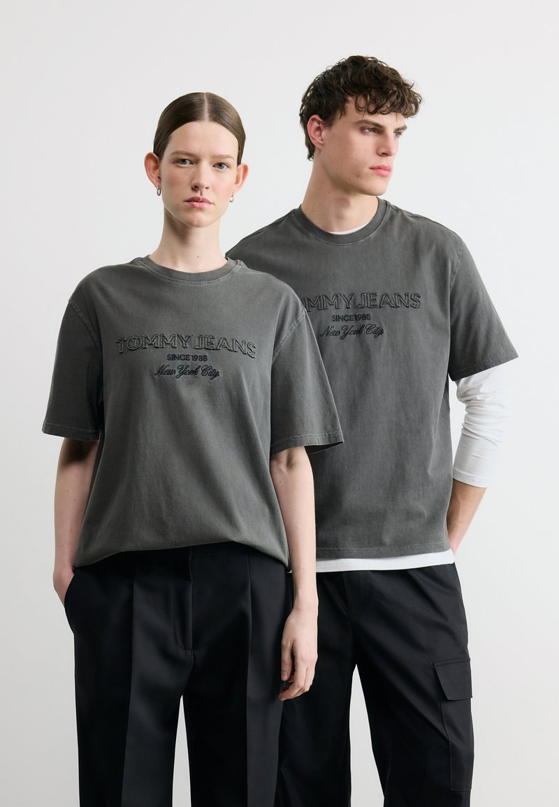 Δύο μοντέλα φοράνε ταιριαστά ξεθωριασμένα μαύρα t-shirts Tommy Jeans και μαύρο παντελόνι, με φόντο απλό λευκό.