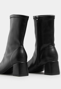 Czarne botki za kostkę wykonane z gładkiej skóry, z zaokrąglonym noskiem, blokowym obcasem i detalem w postaci zamka błyskawicznego z boku; elegancki design z przeszyciami.