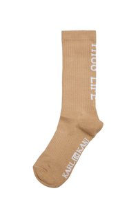 Beige ribbad socka med vitt "LIFE" textdesign och "KARL KANI"-logotyp vid vristen. Tillverkad av mjukt, elastiskt material för komfort.