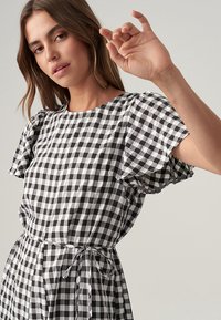 Black and white checked dress with short ruffled sleeves, a round neckline, and a fitted waist tied with a matching belt. Smooth fabric texture.
