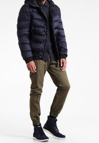 Granatowa pikowana kurtka z kapturem, zapinana na guziki, zestawiona z oliwkowozielonymi, zwężanymi spodniami oraz granatowymi wysokimi trampkami na sznurowadła.