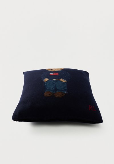 Μαξιλάρι σε ναυτικό μπλε χρώμα με μια αρκούδα που φοράει τζιν και πουλόβερ με την αμερικανική σημαία στο μπροστινό μέρος και κόκκινα αρχικά "RL" στην γωνία.