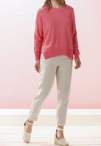 Rosa Pullover mit lockerer Passform und gerippten Bündchen, kombiniert mit hellen Leinenhosen und beigen Keil-Sandalen. Sanfte Texturen und klare Linien.