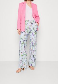 Roze blazer over een witte top, gecombineerd met bloemrijke, lichtblauwe wijde broek. Opvallend bloemmotief met lavendel- en roze accenten.