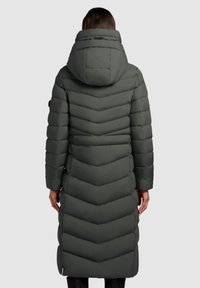 Langer dunkelgrüner Steppmantel mit Chevron-Muster, großer Kapuze und sichtbaren Nahtdetails, der bis zur Mitte der Waden reicht.