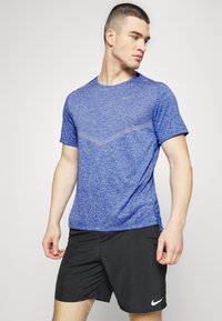 Maglietta atletica blu melangiata con maniche corte, scollatura rotonda e logo Nike discreto. Abbinata a pantaloni corti neri con un logo Nike bianco.