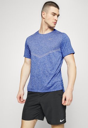 Blau meliertes Sport-T-Shirt mit kurzen Ärmeln, Rundhalsausschnitt und dezentem Nike-Logo. Getragen mit schwarzen Shorts, die einen weißen Nike-Swoosh aufweisen.