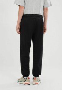 Czarne dresowe spodnie z elastycznym paskiem w talii, dopasowany krój i boczne kieszenie, w połączeniu z beżowymi i zielonymi butami sportowymi.