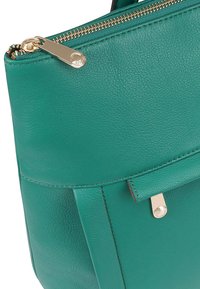 Groene leren handtas met gouden ritssluiting en klein metalen sluitdetail, met close-up van het gestructureerde materiaal en de stiksels.