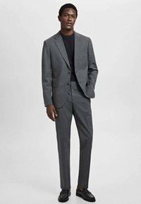 Costume gris sur mesure avec une veste ajustée et un pantalon droit, assorti d'une chemise noire. Texture lisse, matériel minimal, design moderne.