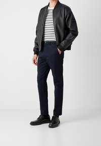 Svart faux läder bomberjacka, vit och marinblå randig t-shirt, mörkblå chinos och svarta snörskor. Enkelt design med kontrasterande färger.