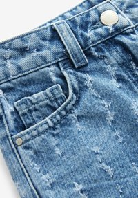 Niebieskie dżinsy z wykończeniem distressed, srebrnym guzikiem i małym detalem kieszonkowym. Tkanina ma teksturowany wygląd z delikatnym blaknięciem.