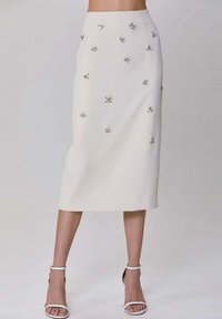 Jupe midi blanche avec des embellissements floraux et des accessoires en métal argenté. Tissu lisse, silhouette ajustée et coupe droite.