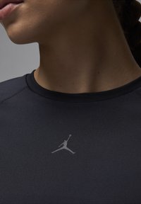 Svart treningsskjorte med rund hals og et reflekterende Air Jordan-logo på brystet. Glatt, tettsittende stoff uten merkbare mønstre.