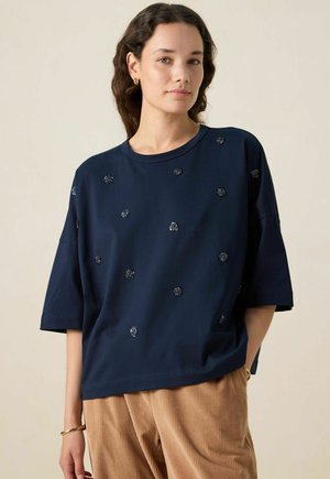 Marineblauwe t-shirt met korte mouwen, voorzien van verspreide decoratieve bloemenaccenten. Relaxte pasvorm met een ronde hals, gecombineerd met beige corduroy broek.